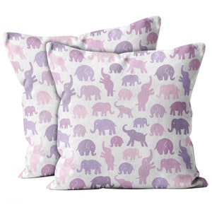 May include: Two square cushions featuring a repeating pattern of purple and pink elephants on a white backdrop. The elephants are depicted in various poses. The cushions are likely made of a soft fabric, suitable for a bedroom or living room.