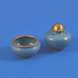 May include: A pair of antique salt and pepper shakers. The shakers are blue with a detailed pattern and gold-coloured accents. The salt shaker has a lid with holes. The bowl has a copper-coloured rim and a green interior.