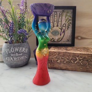 May include: A wooden statue of a woman holding a bowl on her head. The statue is painted in rainbow colors with gold accents. The woman is wearing a skirt with a lotus flower design.