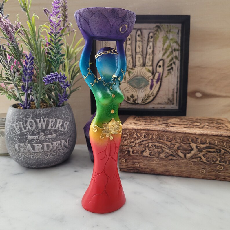 May include: A wooden statue of a woman holding a bowl on her head. The statue is painted in rainbow colors with gold accents. The woman is wearing a skirt with a lotus flower design.