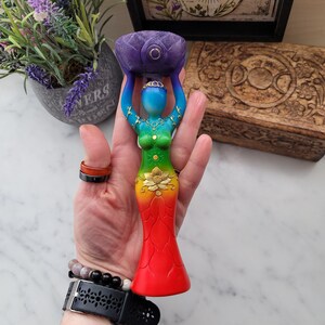 May include: A rainbow colored wooden goddess statue with a lotus flower on her head and a gold lotus flower on her stomach. She is holding a purple lotus flower bowl in her hands.