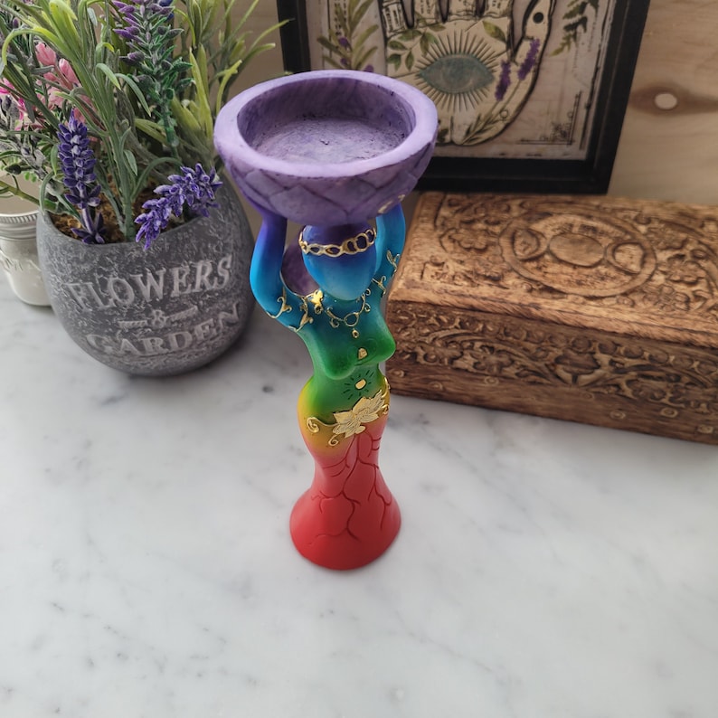May include: A rainbow colored resin statue of a woman holding a purple bowl on her head. The bowl has a gold trim and is designed to hold incense or candles.
