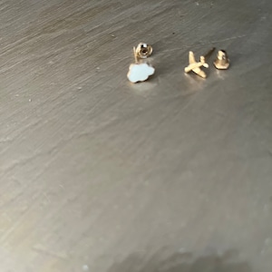 May include: A set of three gold-toned earrings featuring a white cloud, a small airplane, and a star.