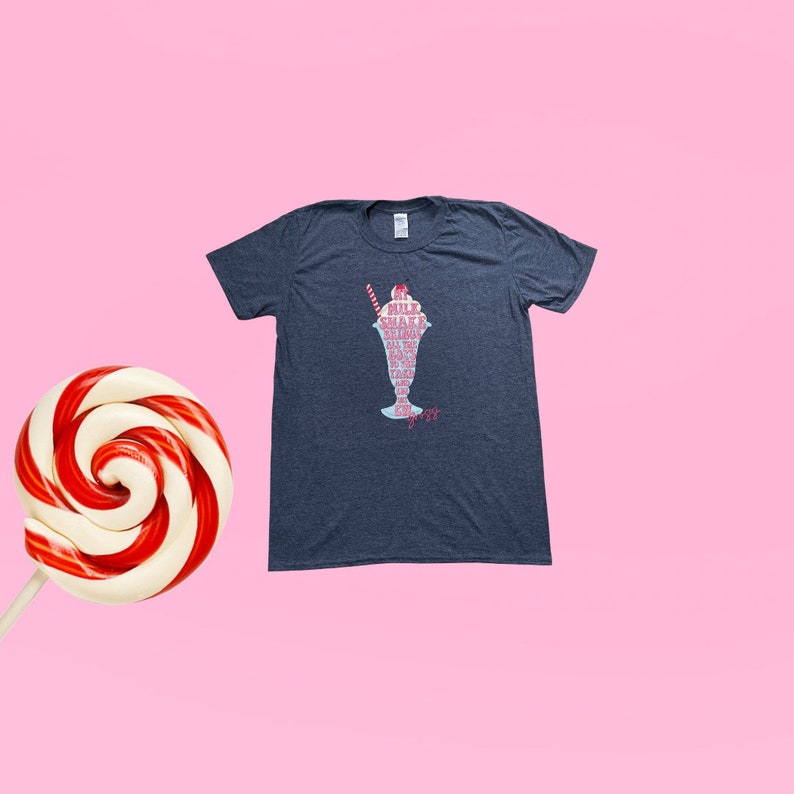 May include: A dark heather grey t-shirt featuring a graphic of a milkshake in a glass with the words "Milk Shake" and "All the things you love" written in pink and white.