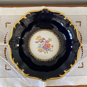 May include: A large, cobalt blue porcelain plate with a gold rim and a white center featuring a floral design. The plate has a scalloped edge.