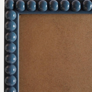 Op de afbeelding: Een vierkante fotolijst met een blauwe kralenrand. De lijst heeft een lichtbruin interieur en een witte achtergrond. De lijst is gemaakt van een glanzend materiaal en is geschikt voor het weergeven van foto's of kunstwerken.