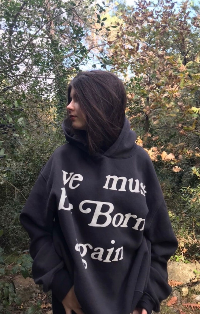 May include: A black hooded sweatshirt with the text "We must be born again" printed in white.