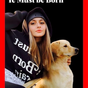 May include: A young woman wearing a black hoodie with the text "Ye Must be Born" in white lettering, a black beanie, and a black and white graphic on the front of the hoodie. She is holding a golden retriever puppy in her arms.