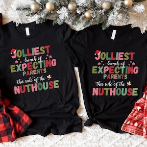 May include: Two black t-shirts with the text "JOLLIEST bunch of EXPECTING PARENTS this side of the NUTHOUSE" in colorful letters. The image also shows red and black plaid pajama pants and red and white patterned pajama pants.