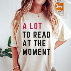 May include: A white t-shirt with the text "A LOT TO READ AT THE MOMENT" printed in black and red.
