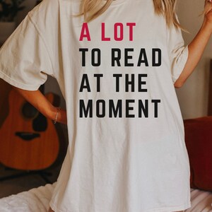May include: A white oversized t-shirt with the text "A LOT TO READ AT THE MOMENT" printed in black with the word "LOT" in pink.