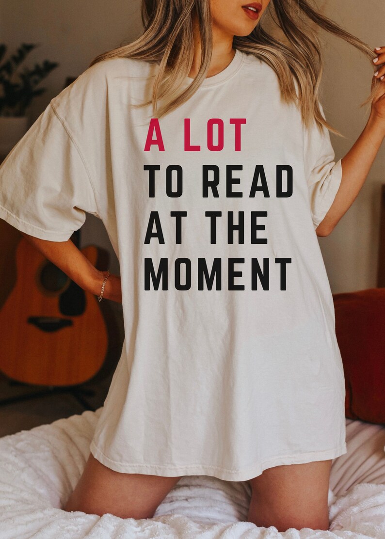May include: A white oversized t-shirt with the text "A LOT TO READ AT THE MOMENT" printed in black with the word "LOT" in pink.