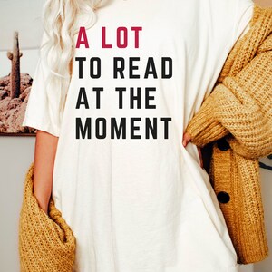 May include: A white t-shirt with the text "A LOT TO READ AT THE MOMENT" printed in black with the word "LOT" in red.