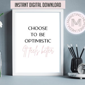 Puede incluir: Imprimible enmarcado en blanco con texto negro que dice "Elige ser optimista Se siente mejor". La impresión está sobre una superficie blanca con un jarrón de flores blancas, un porta lápices negro con lápices y un posavasos de mármol blanco con una esfera de vidrio y un reloj de arena.