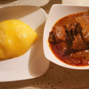 May include: A white plate with a yellow, round, soft food, and a white plate with a red sauce and brown meat.