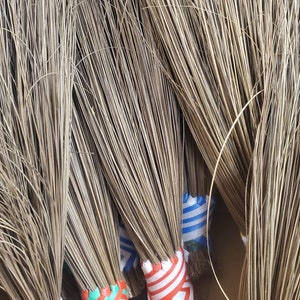 Pode incluir: Um close-up de um feixe de vassouras marrons com faixas coloridas listradas na base. As faixas são azul e branco, vermelho e branco, verde e laranja, e preto e amarelo.