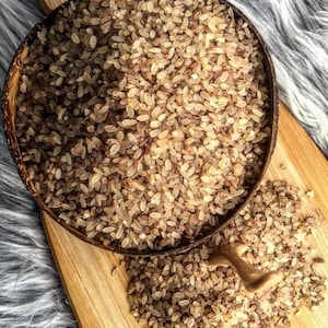 May include: A close-up of a wooden bowl filled with brown rice. The rice is scattered on a wooden surface.