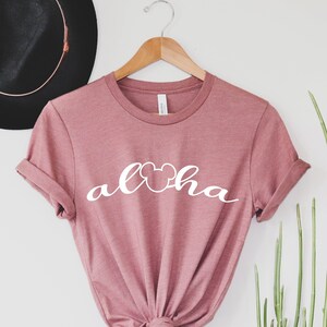 May include: A dusty rose t-shirt with a white graphic that says "Aloha" with a Mickey Mouse head in the "o".