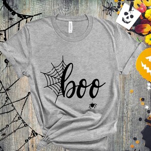 May include: A gray t-shirt with a black spiderweb and the word "boo" in a black cursive font. A small black spider is hanging from the bottom of the "o" in "boo".