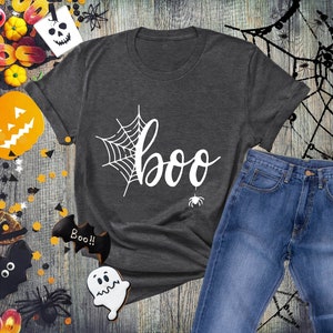 May include: A dark gray t-shirt with a white spiderweb and the word "boo" in a white cursive font. A small white spider is hanging from the bottom of the word "boo".