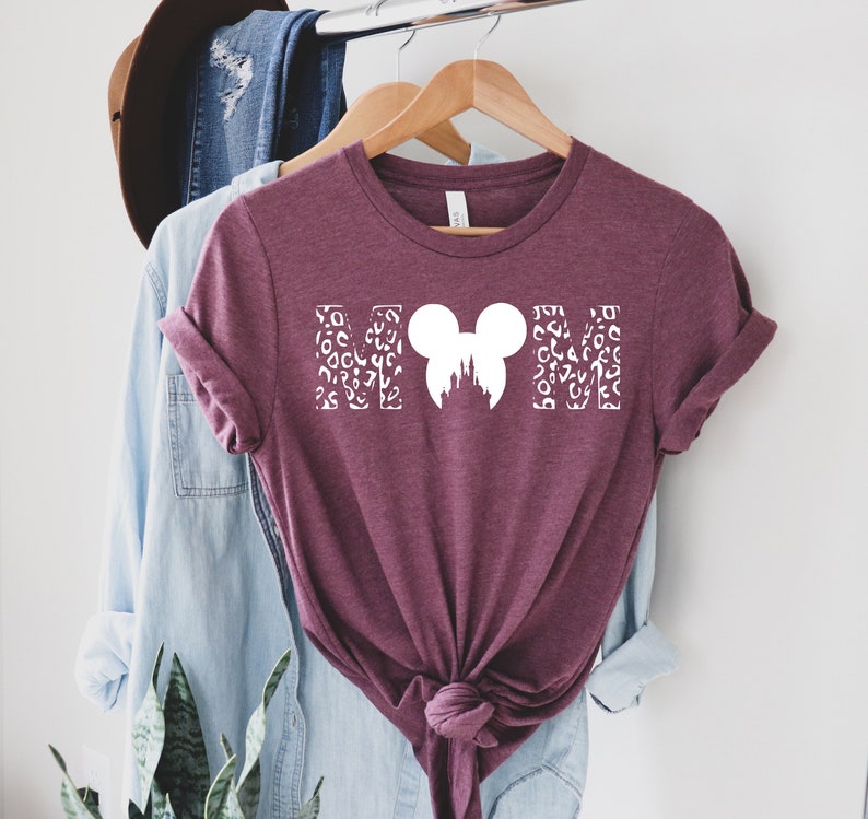 May include: Burgundy t-shirt with a white graphic of the word "MOM" with a Mickey Mouse head and the silhouette of Cinderella's castle in the middle.