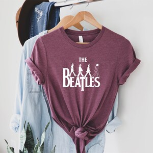 May include: A maroon t-shirt with a white graphic of the Beatles walking across the street, with the text "THE BEATLES" underneath.