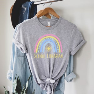 May include: A gray t-shirt with a rainbow and sun graphic and the text "SCHOOL LIBRARIAN" in yellow.