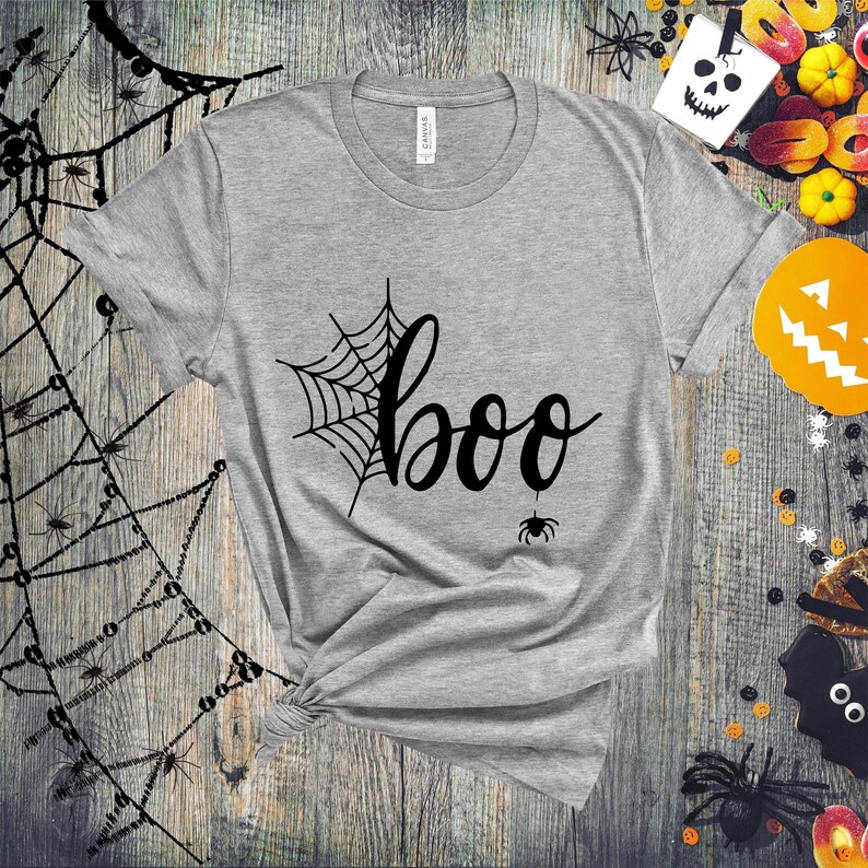May include: A gray t-shirt with a black spiderweb and the word "boo" in a black cursive font. A small black spider is hanging from the bottom of the "o" in "boo".