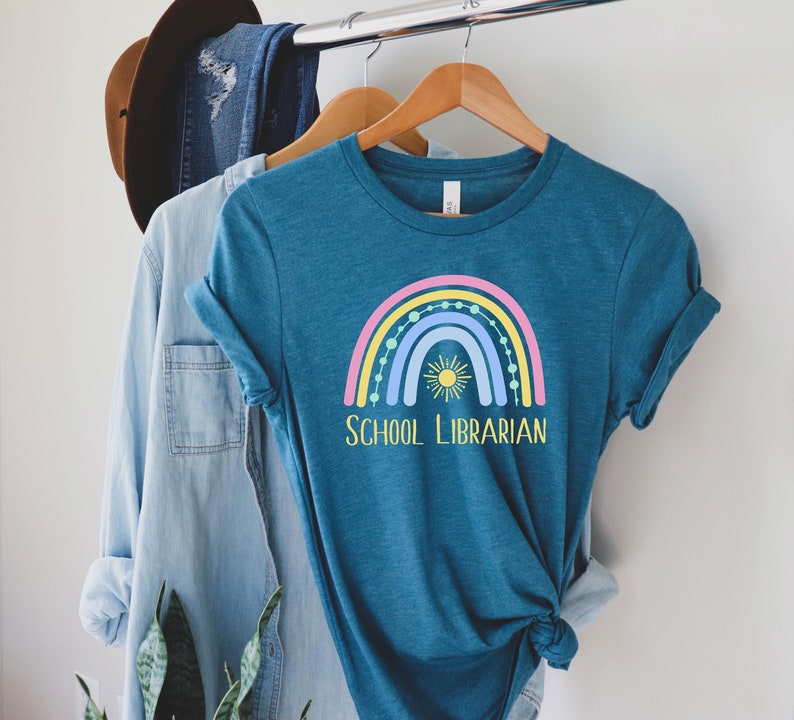 May include: A teal blue t-shirt with a rainbow and sun graphic and the text "SCHOOL LIBRARIAN".