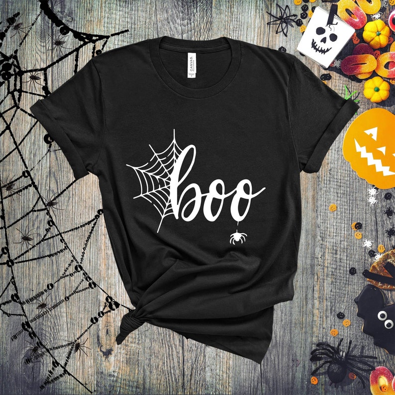 May include: Black t-shirt with a white spiderweb and the word "boo" in a white cursive font. A small white spider hangs from the bottom of the word "boo".