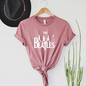 May include: A pink t-shirt with a white graphic of the Beatles walking across the street, with the text "THE BEATLES" underneath.