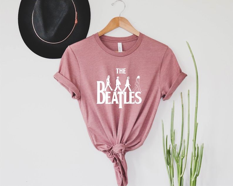 May include: A pink t-shirt with a white graphic of the Beatles walking across the street, with the text "THE BEATLES" underneath.