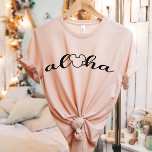 May include: A light pink t-shirt with a black Mickey Mouse head and the word "Aloha" written in a cursive font.