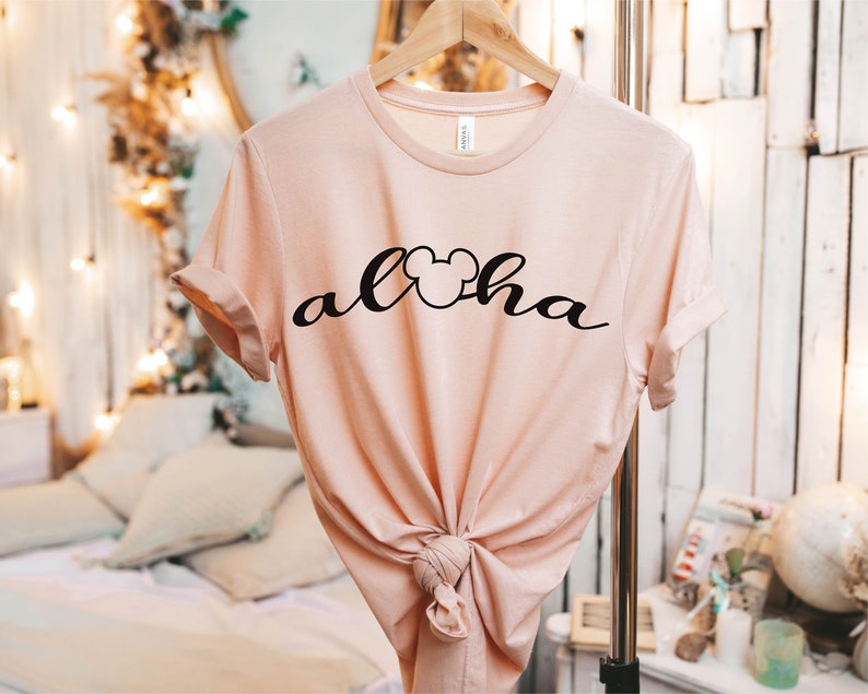 May include: A light pink t-shirt with a black Mickey Mouse head and the word "Aloha" written in a cursive font.