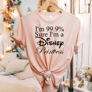 May include: A light pink t-shirt with the text "I'm 99.9% Sure I'm a Disney Princess" printed in black.