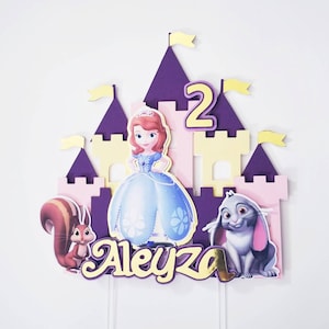May include: Purple and pink castle cake topper with a princess, squirrel, and rabbit. The cake topper also includes the number 2 and the name Aleyza.