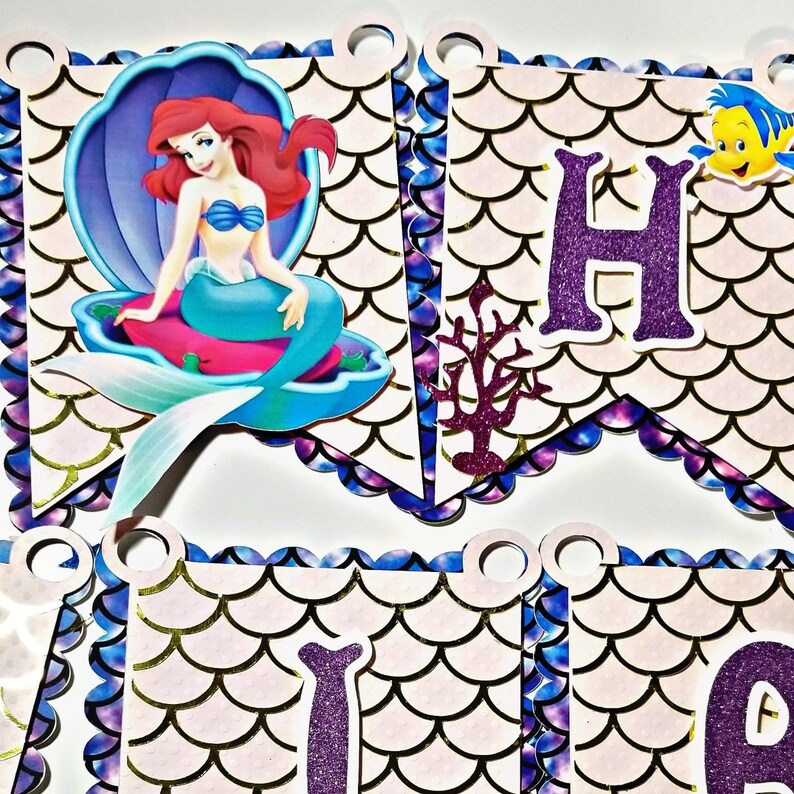 Pu&ograve; includere: Uno striscione di compleanno con una sirena su sfondo viola e blu. Lo striscione presenta una sirena, un cavalluccio marino e le lettere "Happy".