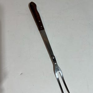 May include: A silver metal fork with a brown wooden handle. The fork has two prongs and is designed for serving food.