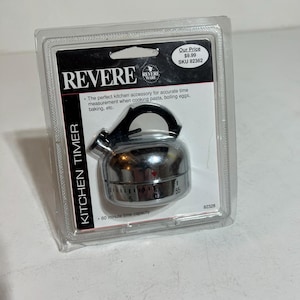 May include: A Revere kitchen timer in a clear plastic package. The timer is shaped like a small kettle with a black handle and a silver-colored body. The packaging includes the text "REVERE" and "KITCHEN TIMER". The timer has a 60-minute capacity.