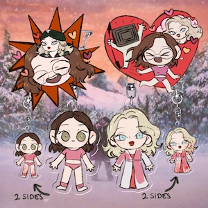 Può includere: Una collezione di portachiavi in acrilico con personaggi in stile cartone animato. Due ciondoli grandi mostrano personaggi in cornici a stella e cuore, mentre quattro piccoli raffigurano figure in abiti rosa. Il testo recita 2 SIDES.