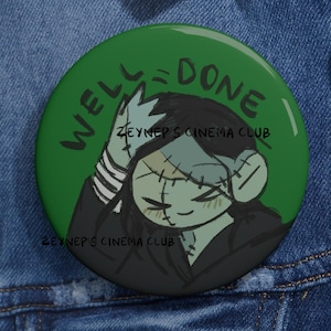 Pode incluir: Um botão redondo verde com as palavras "WELL DONE" em uma fonte estilizada. O botão apresenta uma ilustração de desenho animado de um personagem tipo Frankenstein com o texto "ZEYNEP'S CINEMA CLUB".