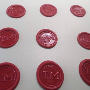 Puede incluir: Varios sellos de cera rojos, cada uno con las letras "TM" dentro de un &oacute;valo. Los sellos est&aacute;n dispuestos sobre una superficie clara, resaltando su dise&ntilde;o y color uniformes. Perfectos para documentos.