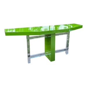 May include: A modern, lime green console table with a glossy finish. The table features a rectangular top supported by clear, geometric legs and a central vertical support. The design is minimalist and contemporary.
