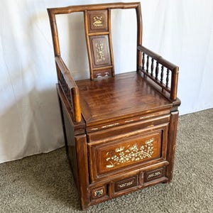 May include: A dark wood chair with a storage compartment and drawers. The chair has a high back and intricate carvings. The chair is decorated with mother of pearl inlay.