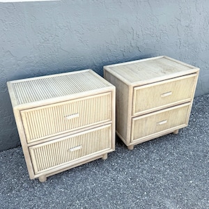 May include: A pair of light beige nightstands featuring a reeded texture on the exterior surfaces. Each nightstand is constructed with two drawers, each equipped with a single horizontal handle, and is supported by four small, low-profile feet.