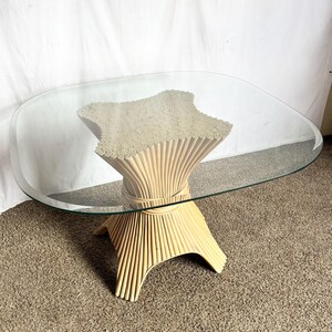 May include: A vintage coffee table with a clear oval glass top. The base is made of light beige bamboo, with a starburst design in the center. The table is approximately 30 inches long and 18 inches tall.