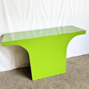 May include: A modern, lime green console table with a glossy finish. The table has a unique, curved design on one side, and a rectangular top. The table is approximately 48 inches long, 16 inches wide, and 30 inches high.