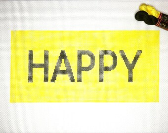 May include: A needlepoint canvas with the word "HAPPY" stitched in black on a yellow background. The canvas is white with a grid pattern. Two spools of yellow and black thread are in the upper right corner.