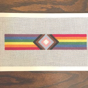 May include: A rainbow pride flag with a brown, pink, white, and blue diamond in the center.