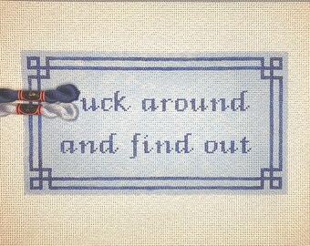 May include: A blue and white cross-stitch sampler with the phrase "Luck around and find out" in a blue frame.